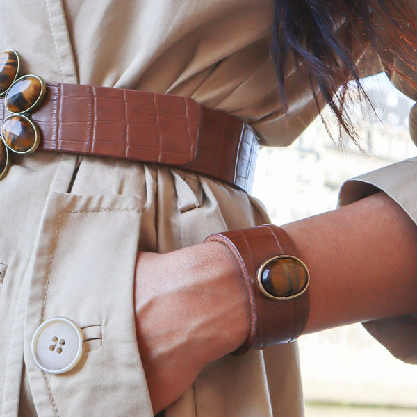Femme élégante portant à la taille une ceinture de cuir marron et au poignet un bracelet serti d'une pierre naturelle