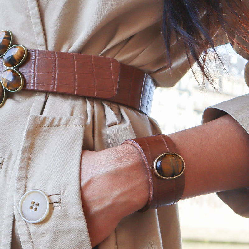 Femme élégante portant à la taille une ceinture de cuir marron et au poignet un bracelet serti d'une pierre naturelle