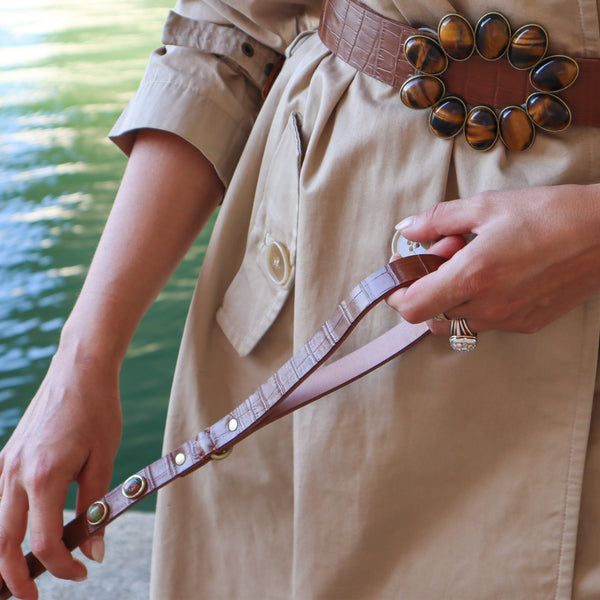 Laisse marron caramel tenue en main par une femme portant une ceinture de cuir caramel et sertie de pierres œil de tigre